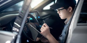 Man in hat and glasses at steering wheel using tablet to check and maintain vehicle
