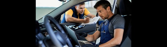 Man with laptop in passenger seat and man with clipboard checklist outside installing telematics